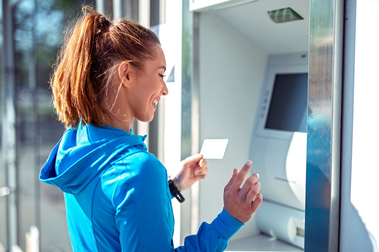 Junge Frau steht im Sportoutfit vor einem Geldautomaten