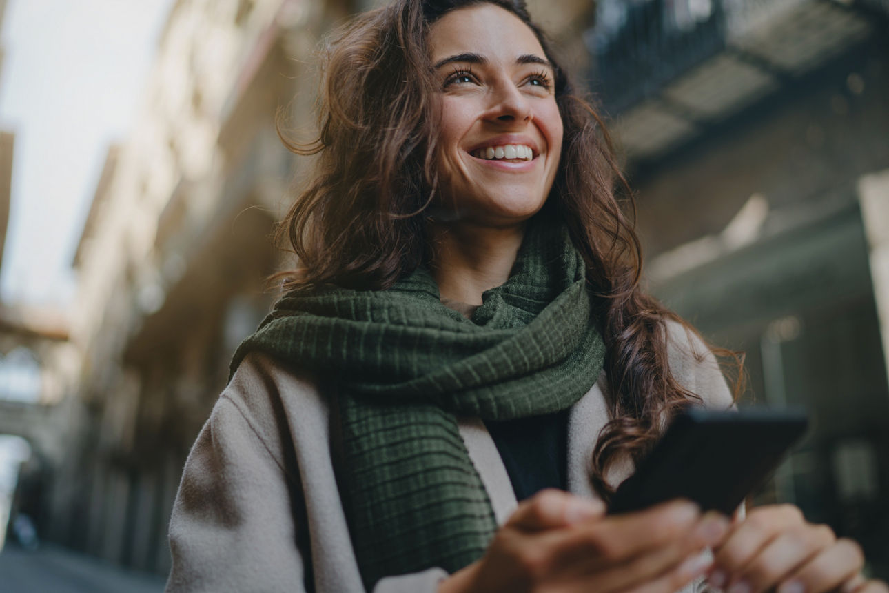 Eine Frau mit Schal hält ein Telfon in der Hand