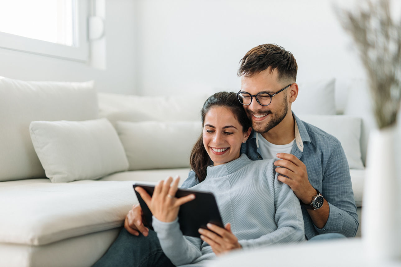 Ein Pärchen sitzt auf einem Sofa und schaut sich online etwas an.