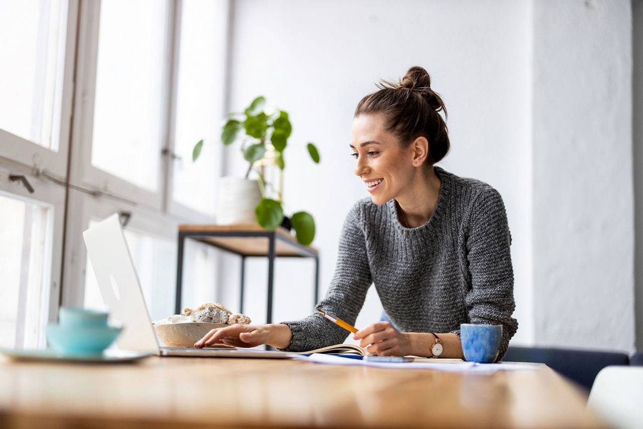 Frau die an ihrem Tisch sitzt und ihr Banking am Laptop im OnlineBanking macht.
