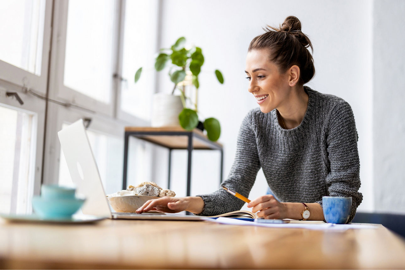 Frau die an ihrem Tisch sitzt und ihr Banking am Laptop im OnlineBanking macht.