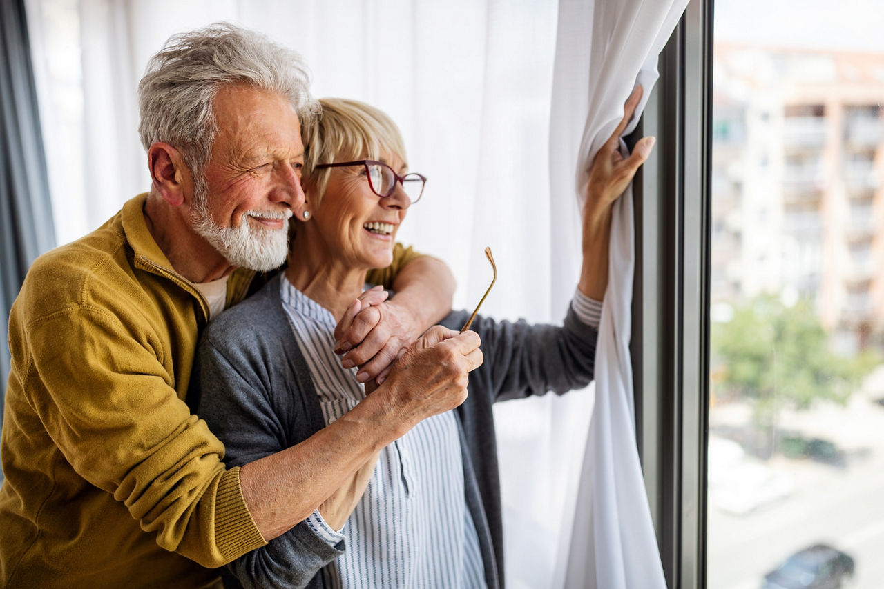 Glückliches älteres Paar das am Fenster steht und rausguckt