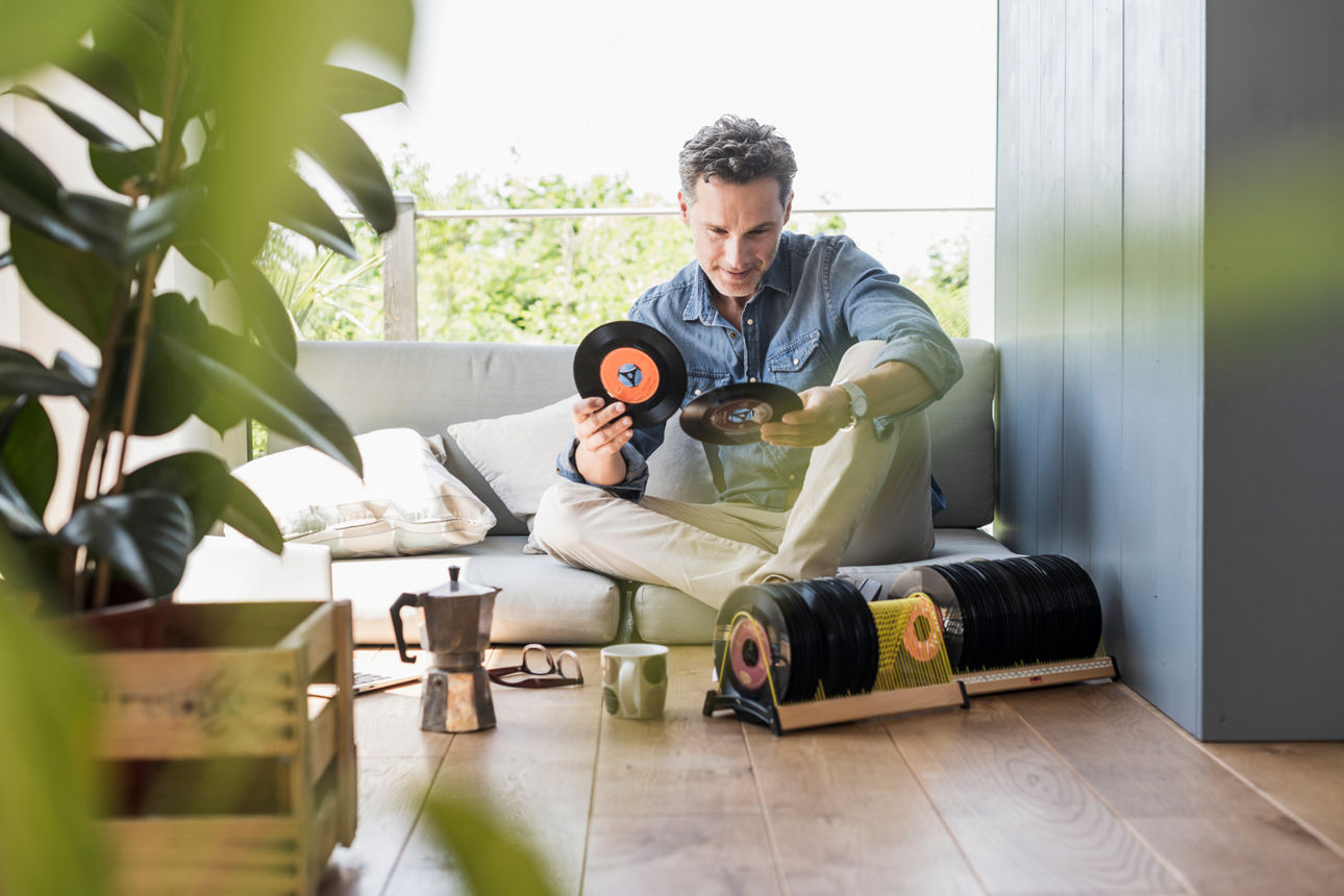 Ein junger Mann sitzt zu Hause auf dem Fußboden und schaut sich Singleschallplatten an.