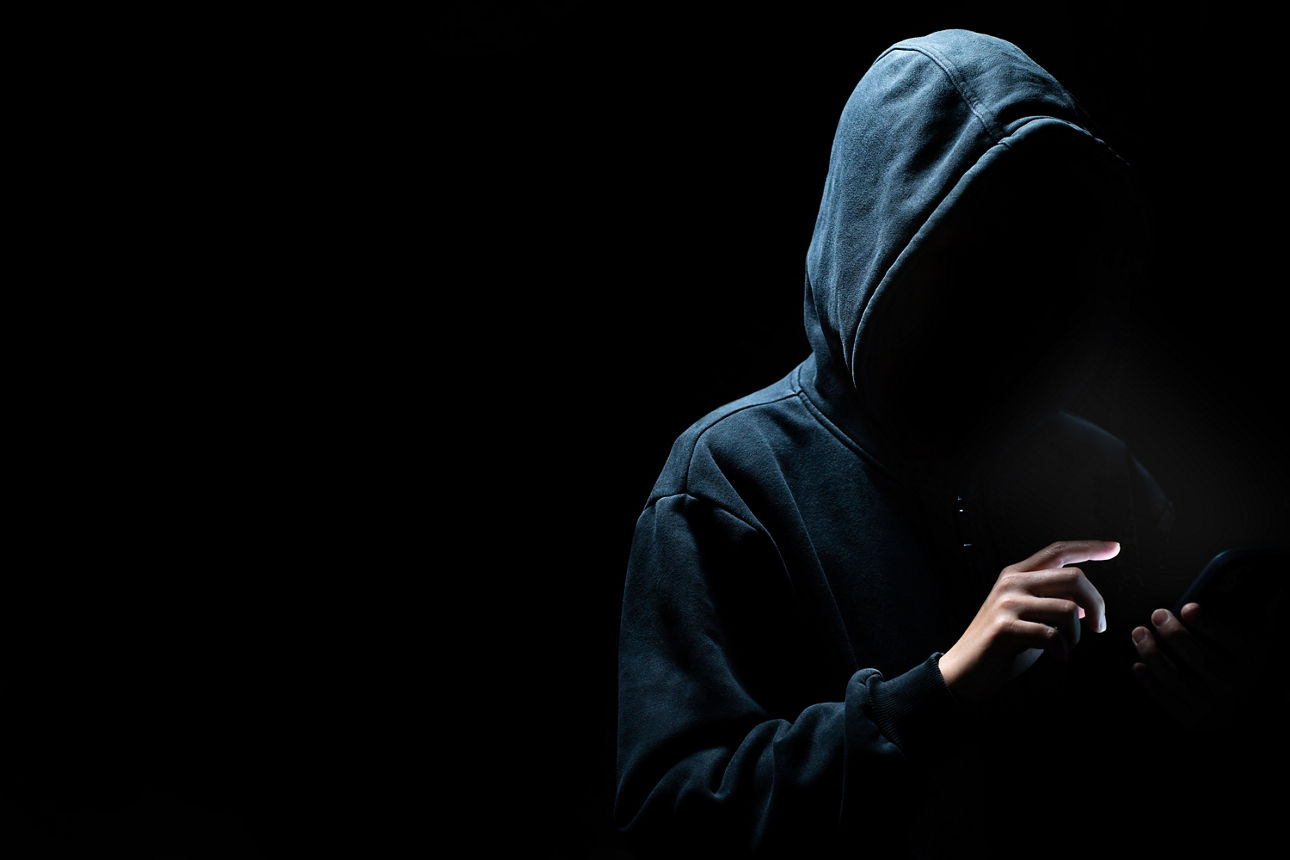 Person mit Kapuzenpulli benutzt das Handy. Das Gesicht ist nicht zu erkennen.