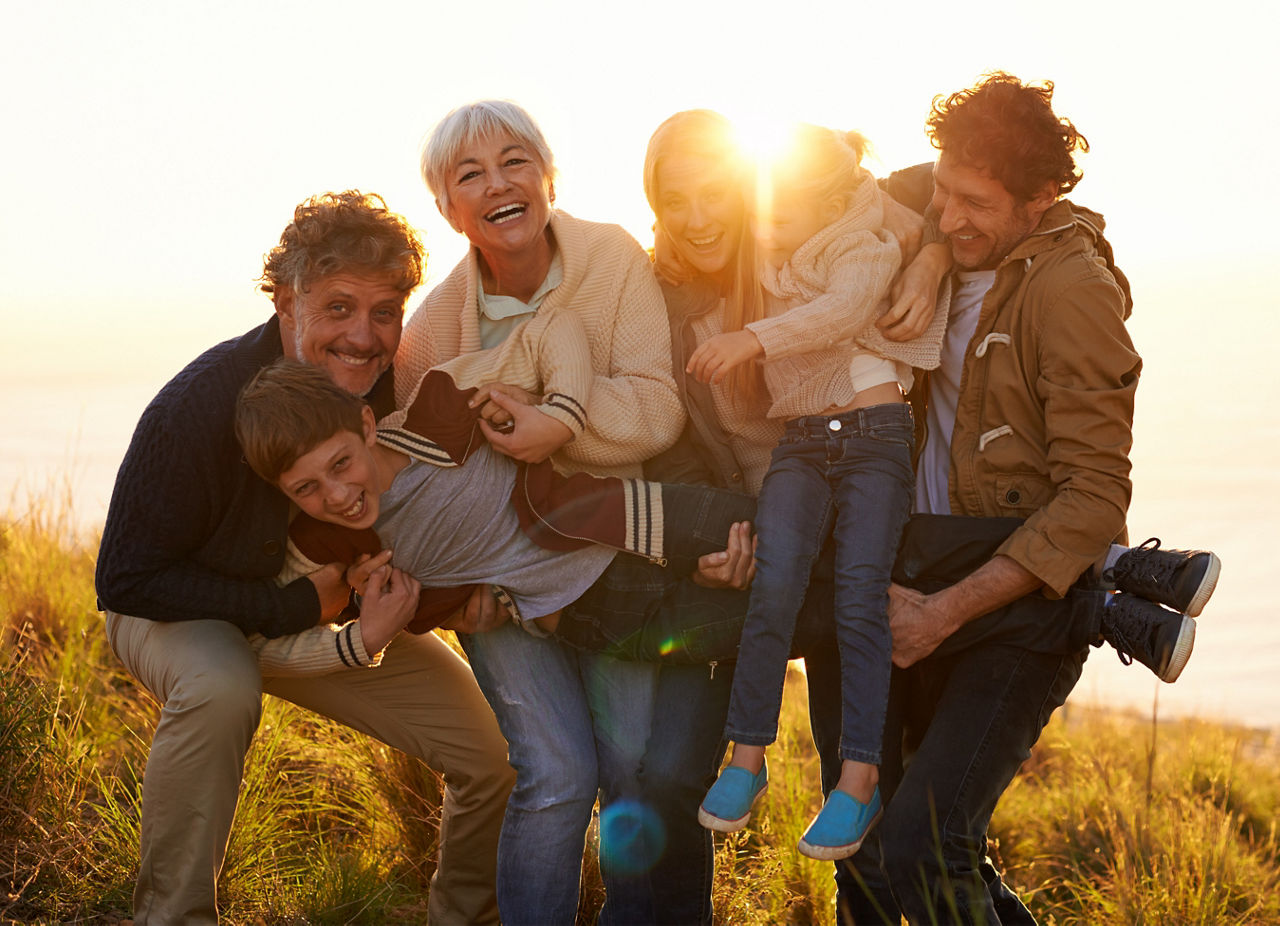 Personen aus drei Generationen stehen freudig beieinander, dahinter der Sonnenaufgang