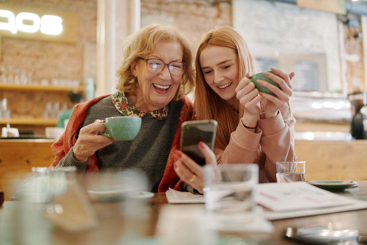 Senorin mit Enkelin im Cafe schauen lachend aufs Handy