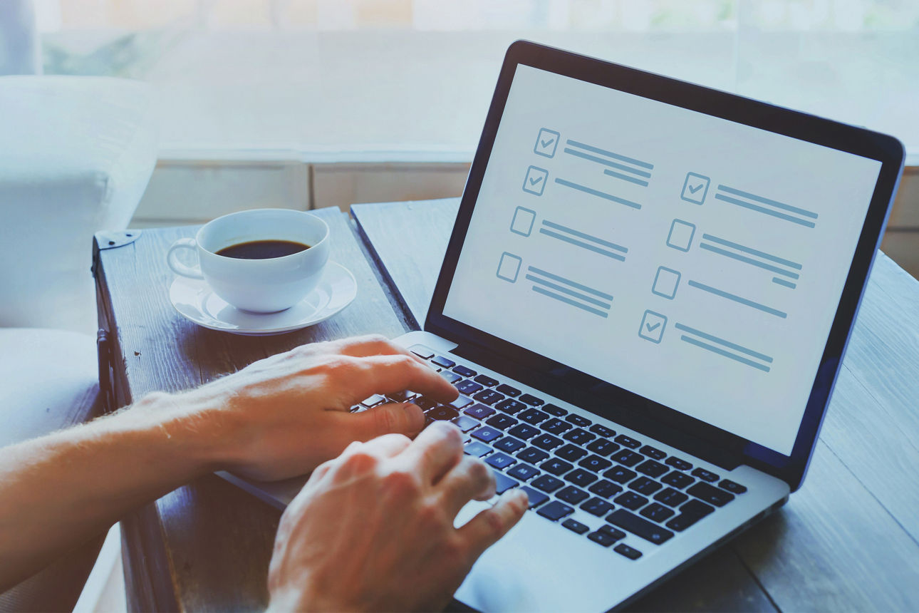  zwei Hände tippen auf einer Laptoptastatur daneben steht eine Tasse Kaffee