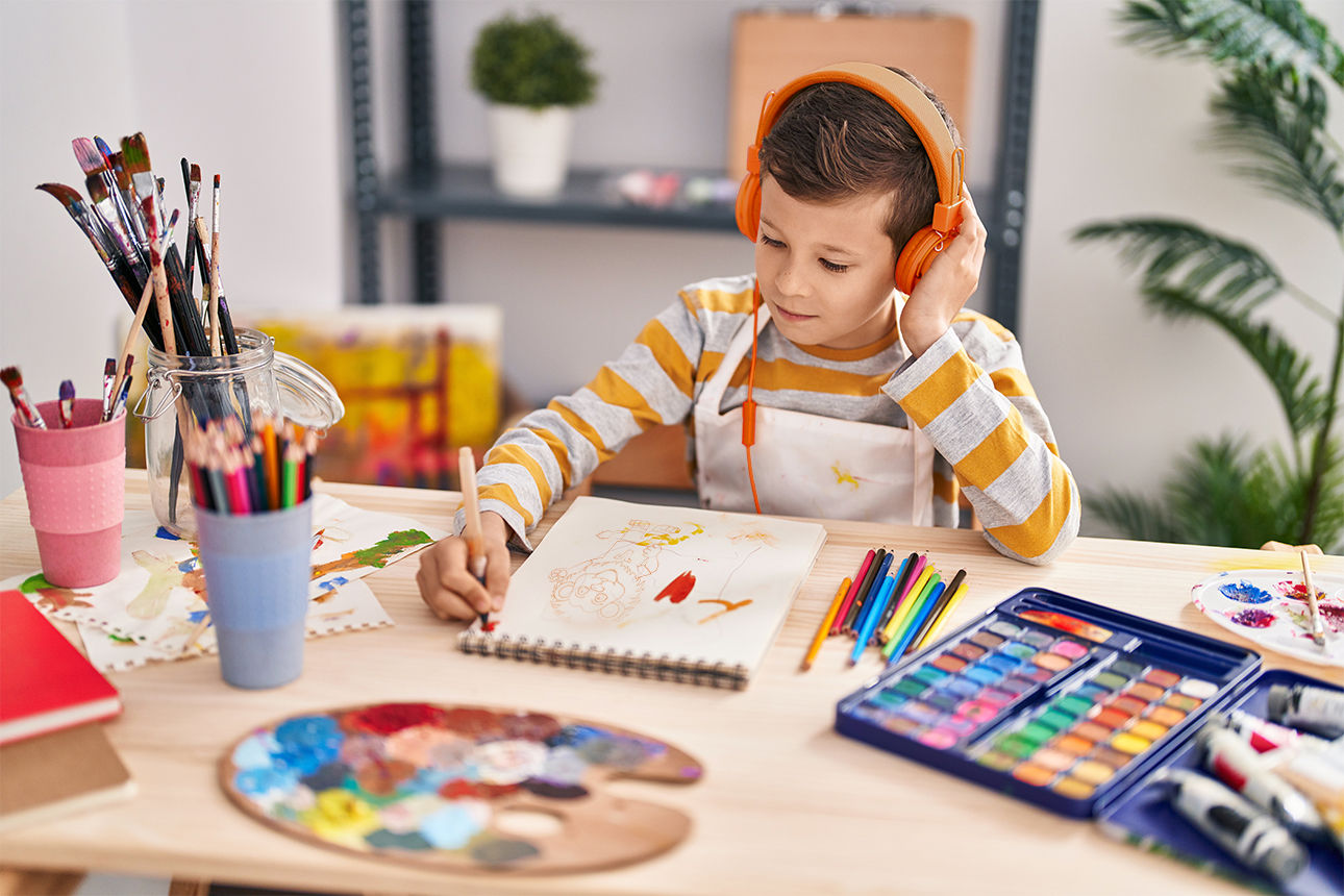 Junge malt ein Bild und hört dabei mit seinen Kopfhörern Musik