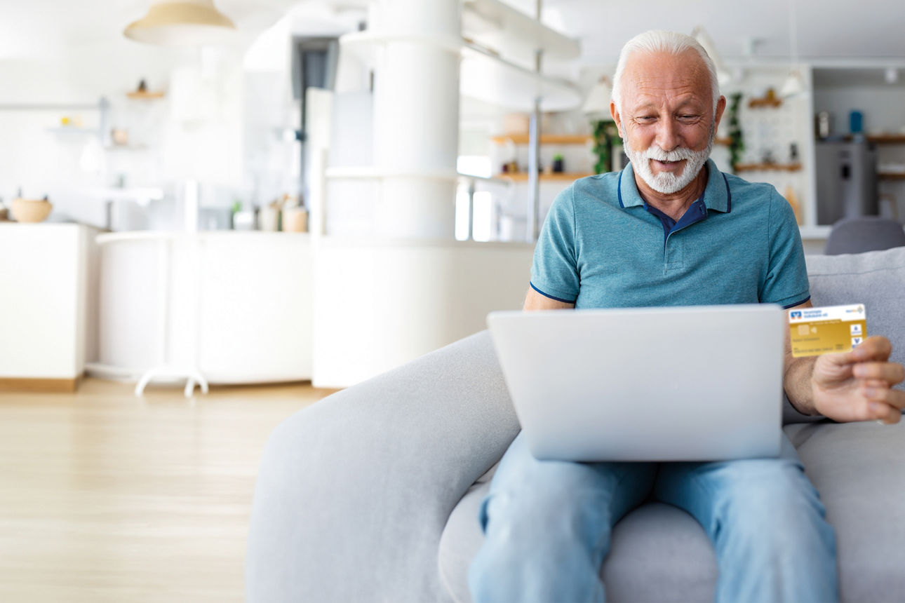 Mature man using laptop, holding plastic credit or debit card, senior grey haired customer making secure internet payment, shopping or browsing online banking service, entering information
