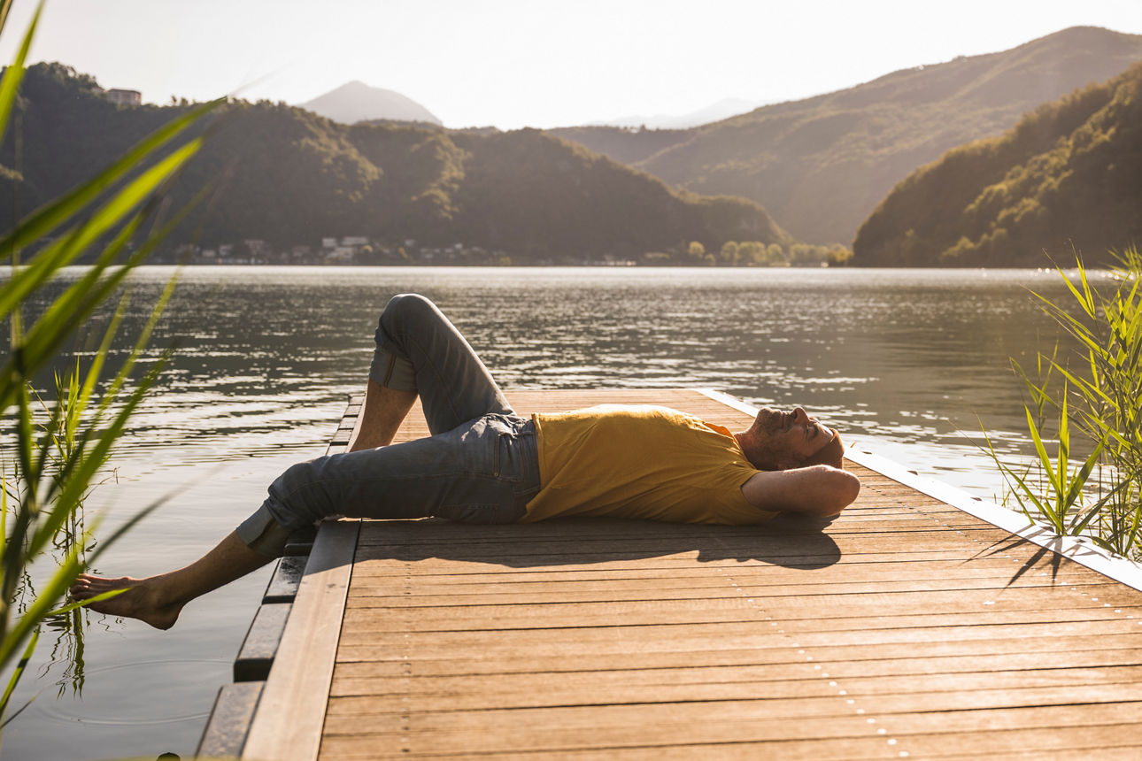 Mature man relaxing on jetty over lake by mountains - VermögensManager
