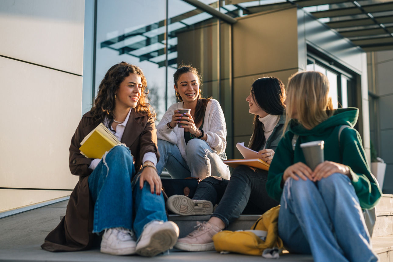 Eine Gruppe Studentinnen sitzt auf einer Treppe und unterhält sich.