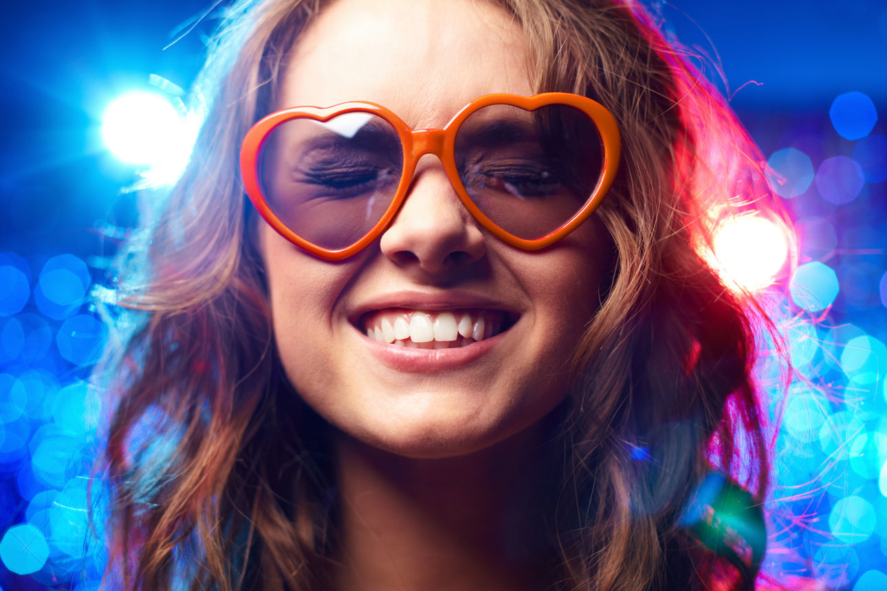 Frau mit oranger Sonnenbrille in Herzform lächelt in die Kamera.