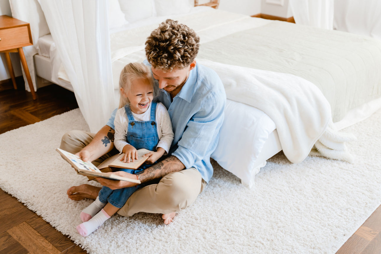 Junger Vater und kleine Tochter lesen gemeinsam zu Hause ein Buch.