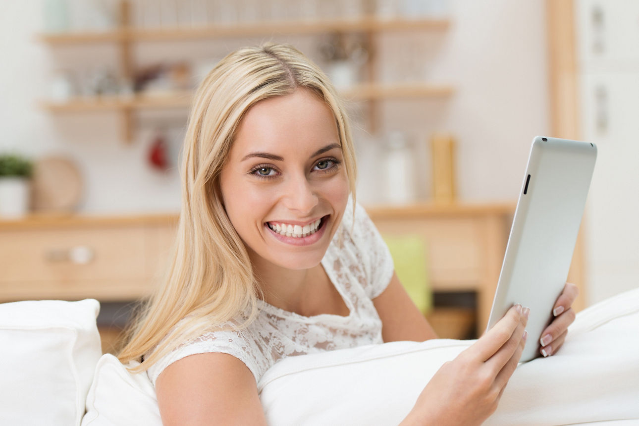 Frau hält lächelnd ein Tablet in der Hand.