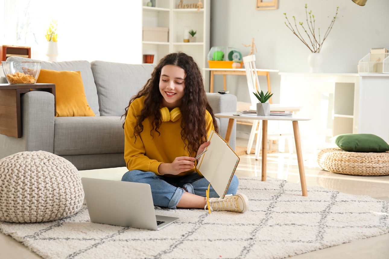 Ein Mädchen sitzt auf dem Wohnzimmerboden vor einem Laptop und hält ihren Block hoch