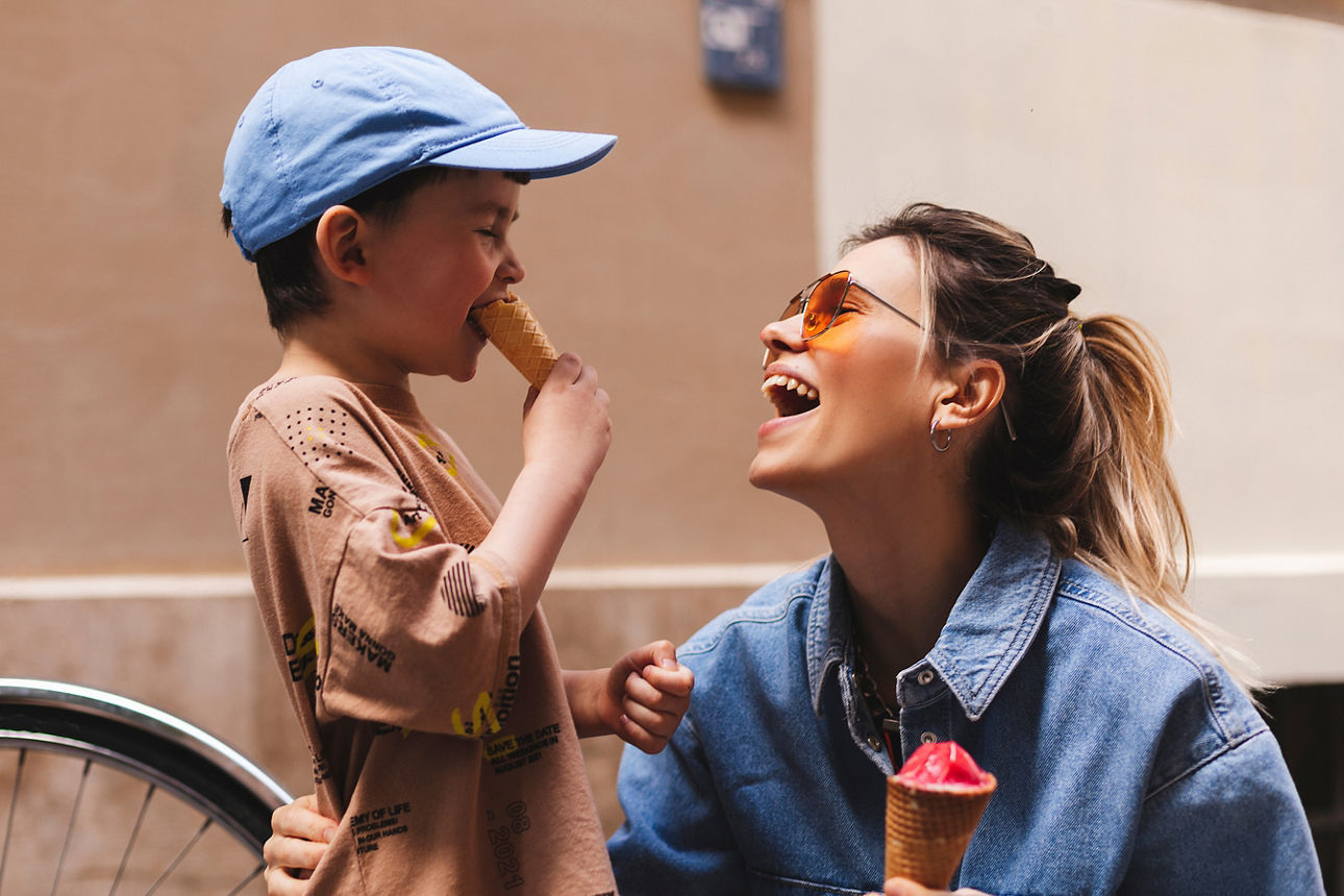 Woman with her son enjoying family time walking in the city together on a sunny day, eating ice cream. Happy family parent wi