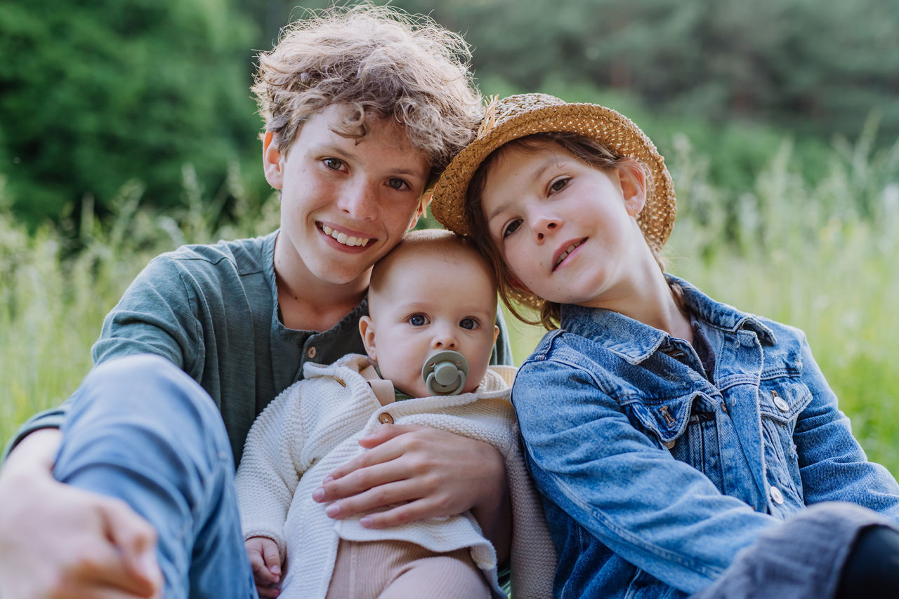 Porträt von drei Kindern, die im Gras sitzen und gemeinsam Spaß haben.