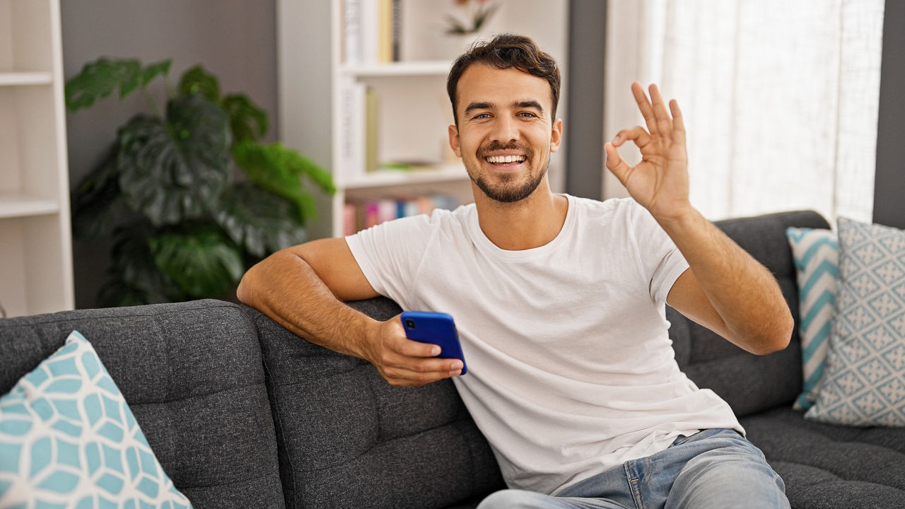 Mann sitzt auf Couch und zeigt mit den Fingern eine Null