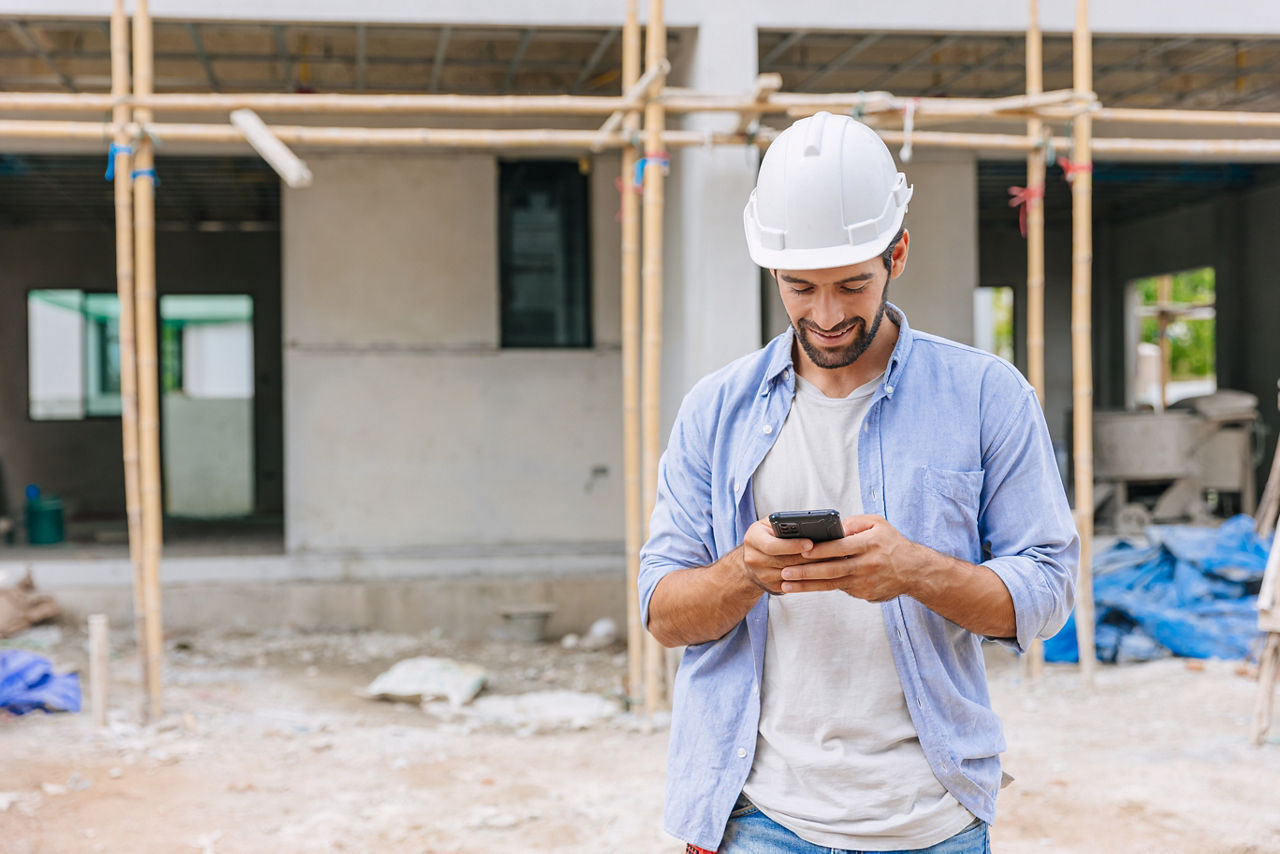 Arbeiter auf Baustelle schaut auf sein Handy und profitiert von den Services & Mehrwerten seiner Bank