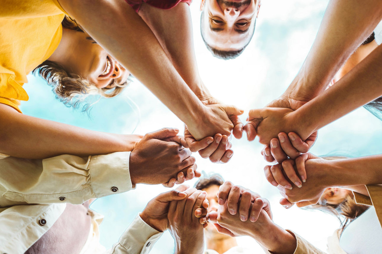 Multi ethnic group of young people holding hands outdoors - Community life style concept with guys and girls hugging together outside - Unity, support and collaboration concept