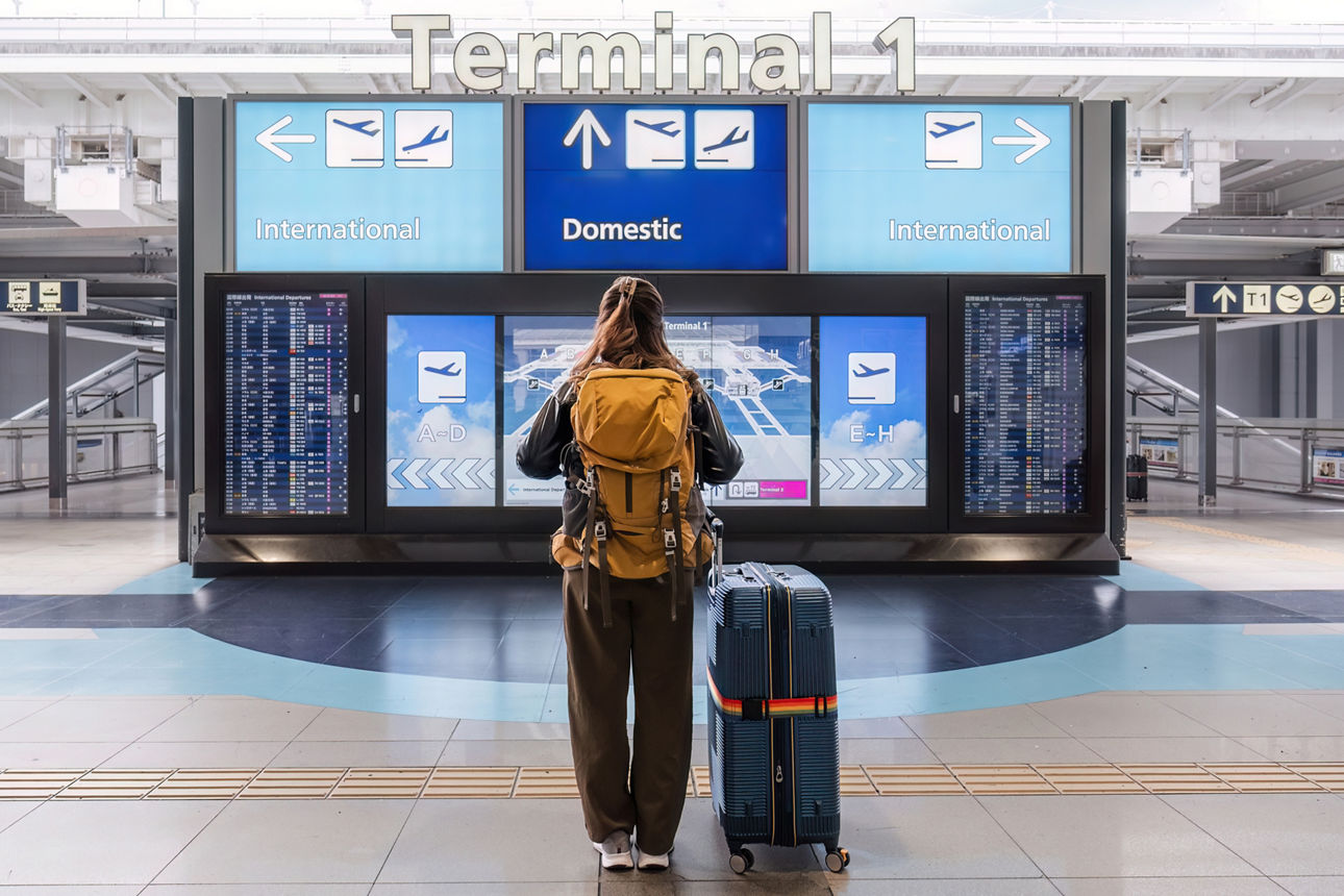 Junge Person auf einem internationalen Flughafen überprüft die Fluginformationen auf der Anzeigetafel.