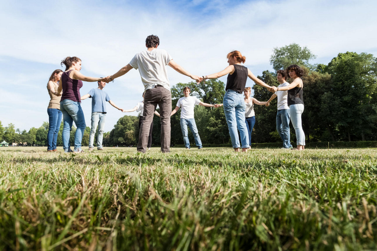 Eine Gruppe steht im Kreis im Park und hält sich an den Händen