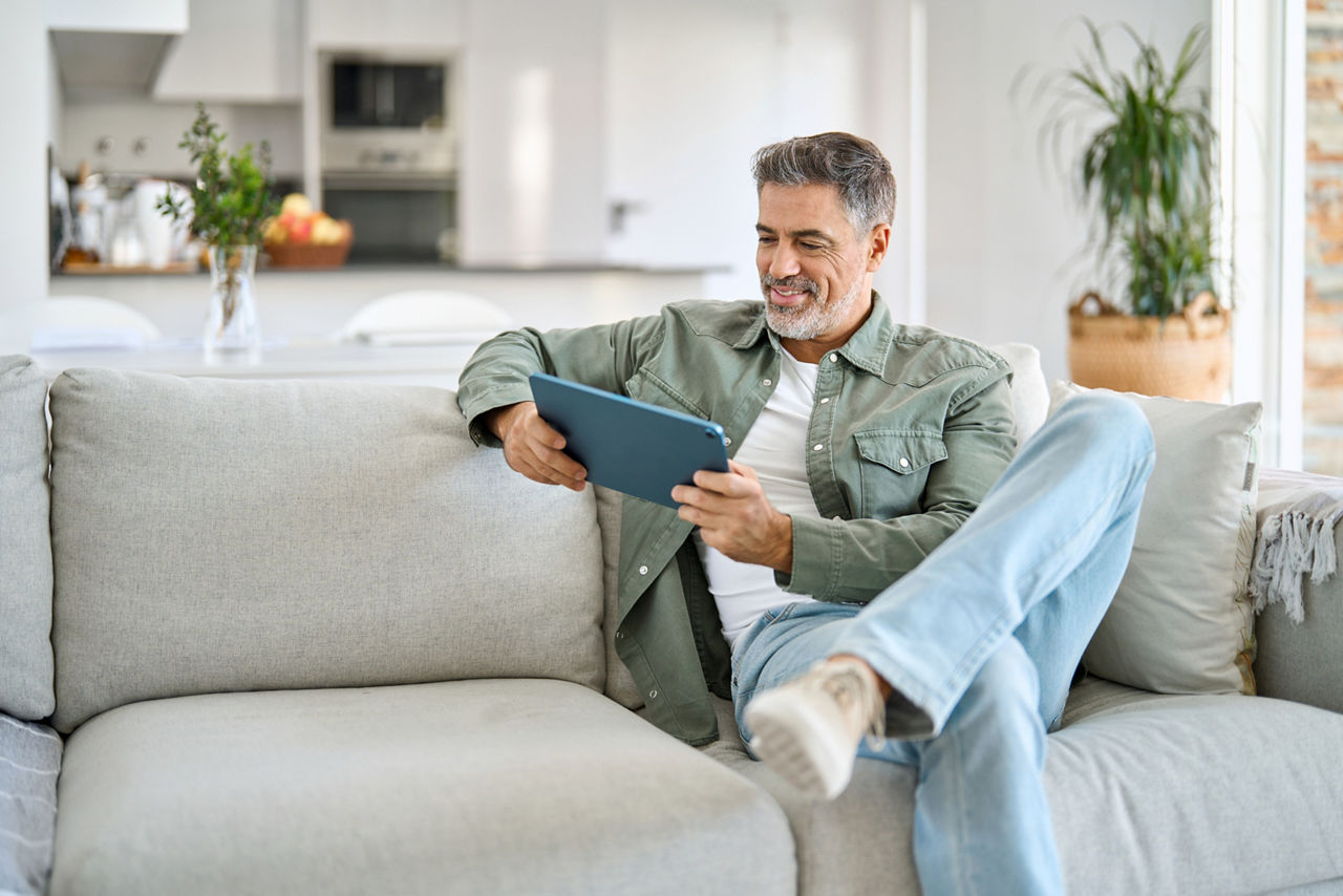 Mann zu Hause auf Sofa mit Tablet lächelnd