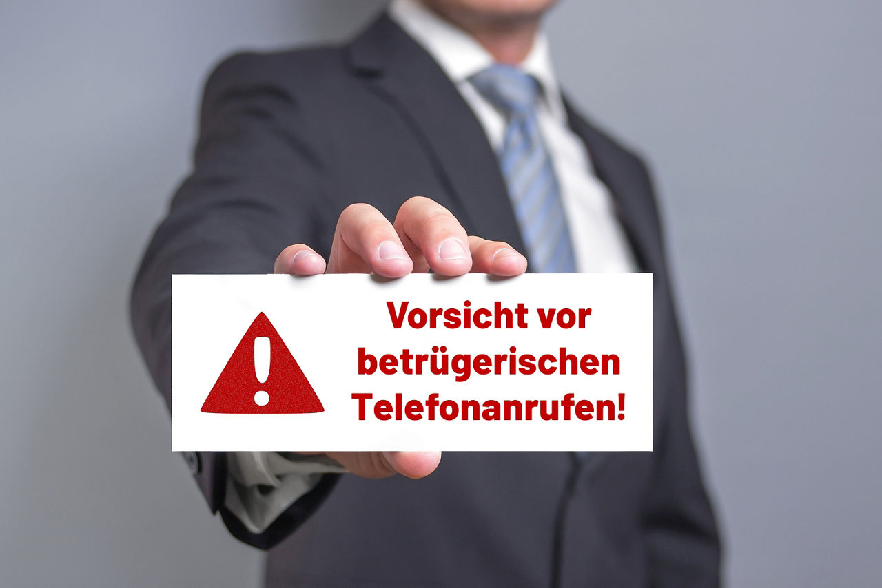Mann hält Schild mit Aufschrift "Vorsicht vor betrügerischen Telefonanrufen!"