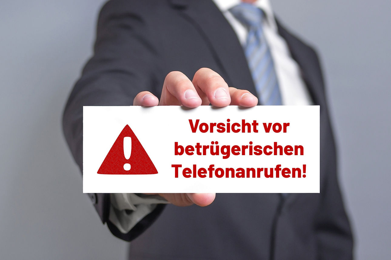 Mann hält Schild mit Aufschrift "Vorsicht vor betrügerischen Telefonanrufen!"