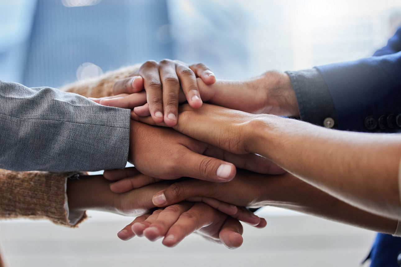 Mehrere Hände liegen übereinander und symbolisieren Zusammenhalt.