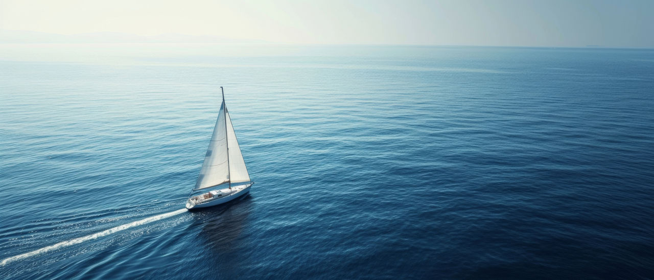 Ein Segelboot mit weißen Segeln fährt auf dem ruhigen, weiten blauen Meer unter einem klaren Himmel und schafft eine ruhige und friedliche Atmosphäre