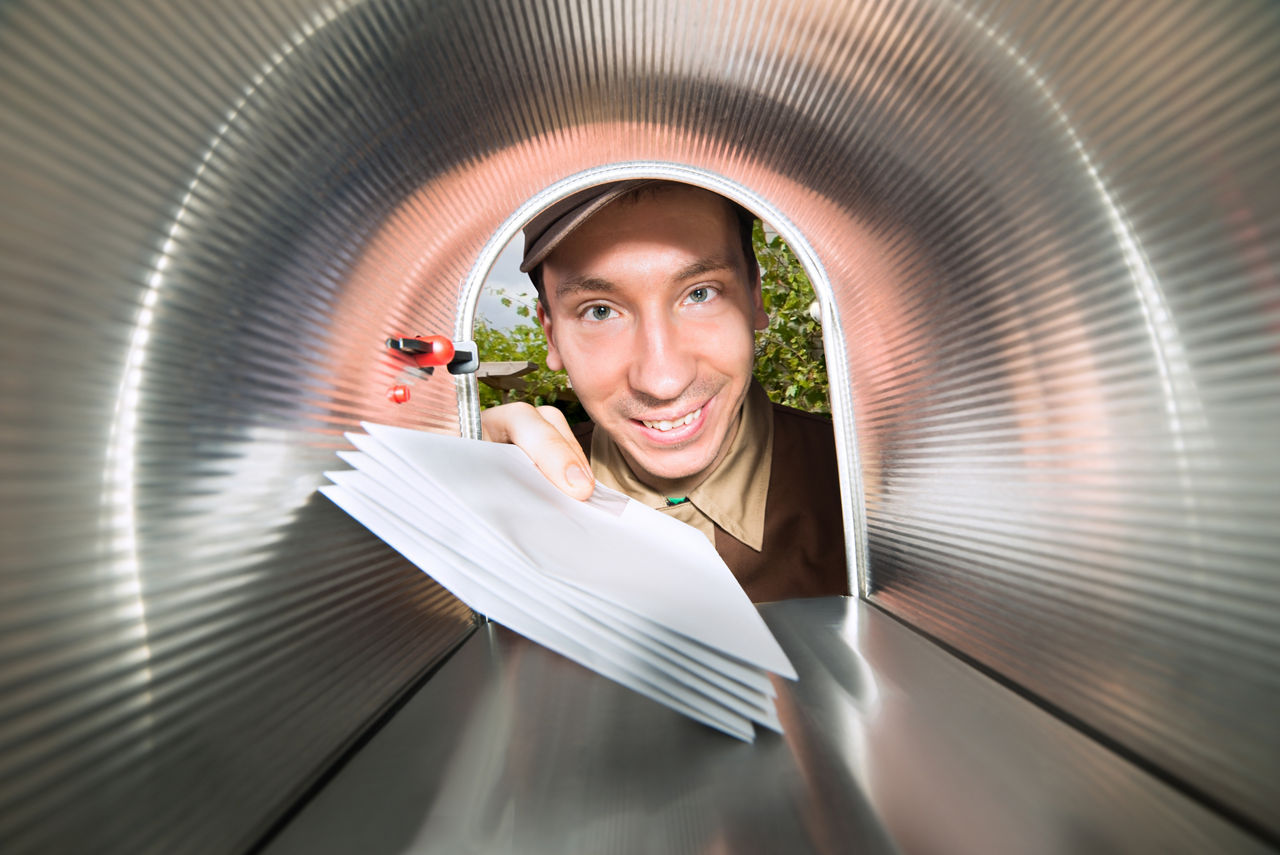 Ein Mann lächelt in schaut in einen silbernen Briefkasten, während er die Post hinein schiebt