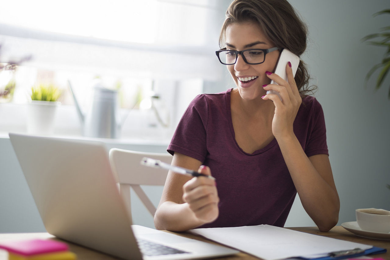 Frau telefoniert mit Handy vor Laptop