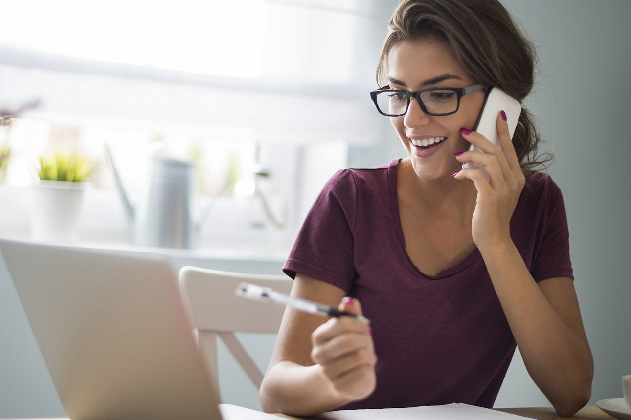 Frau telefoniert mit Handy vor Laptop