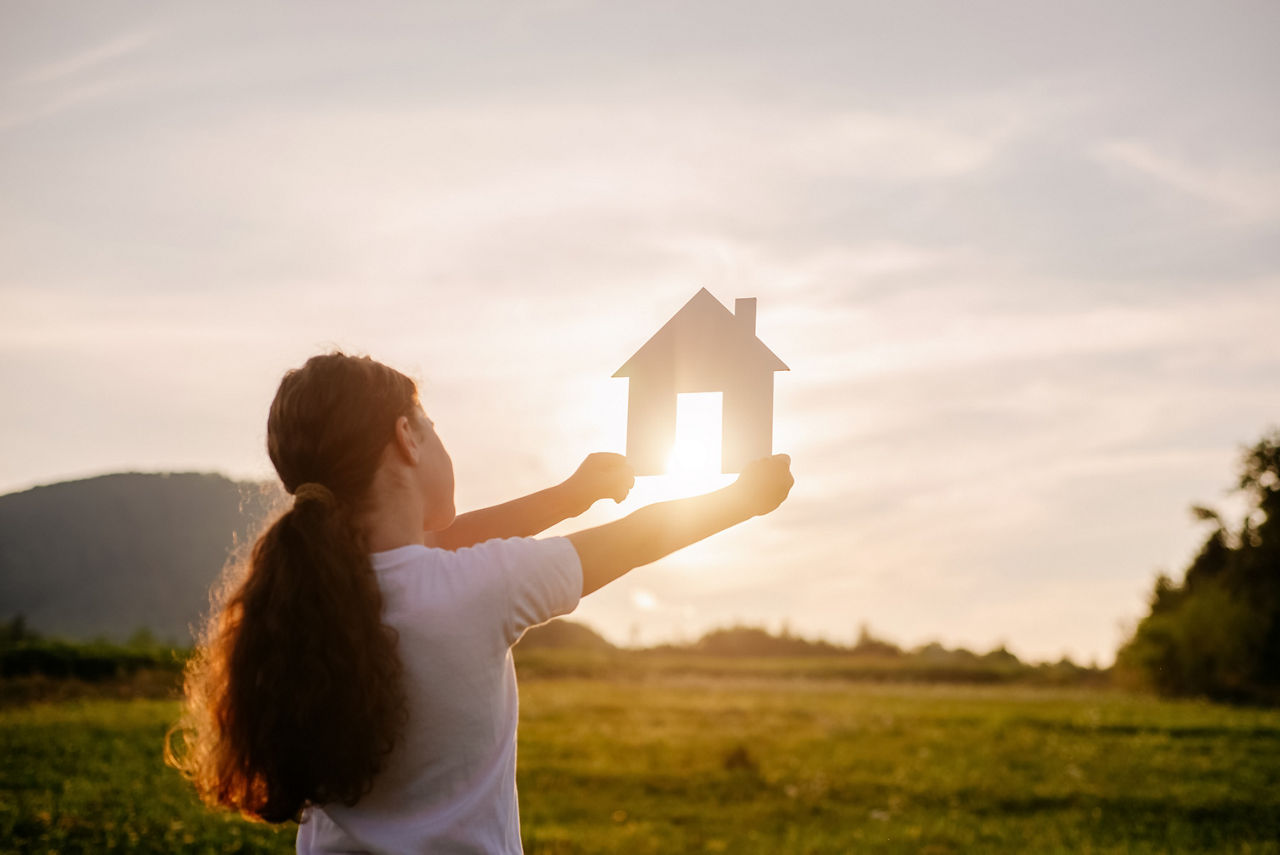 Frau in der Natur hält ein Modellhaus in die Sonne