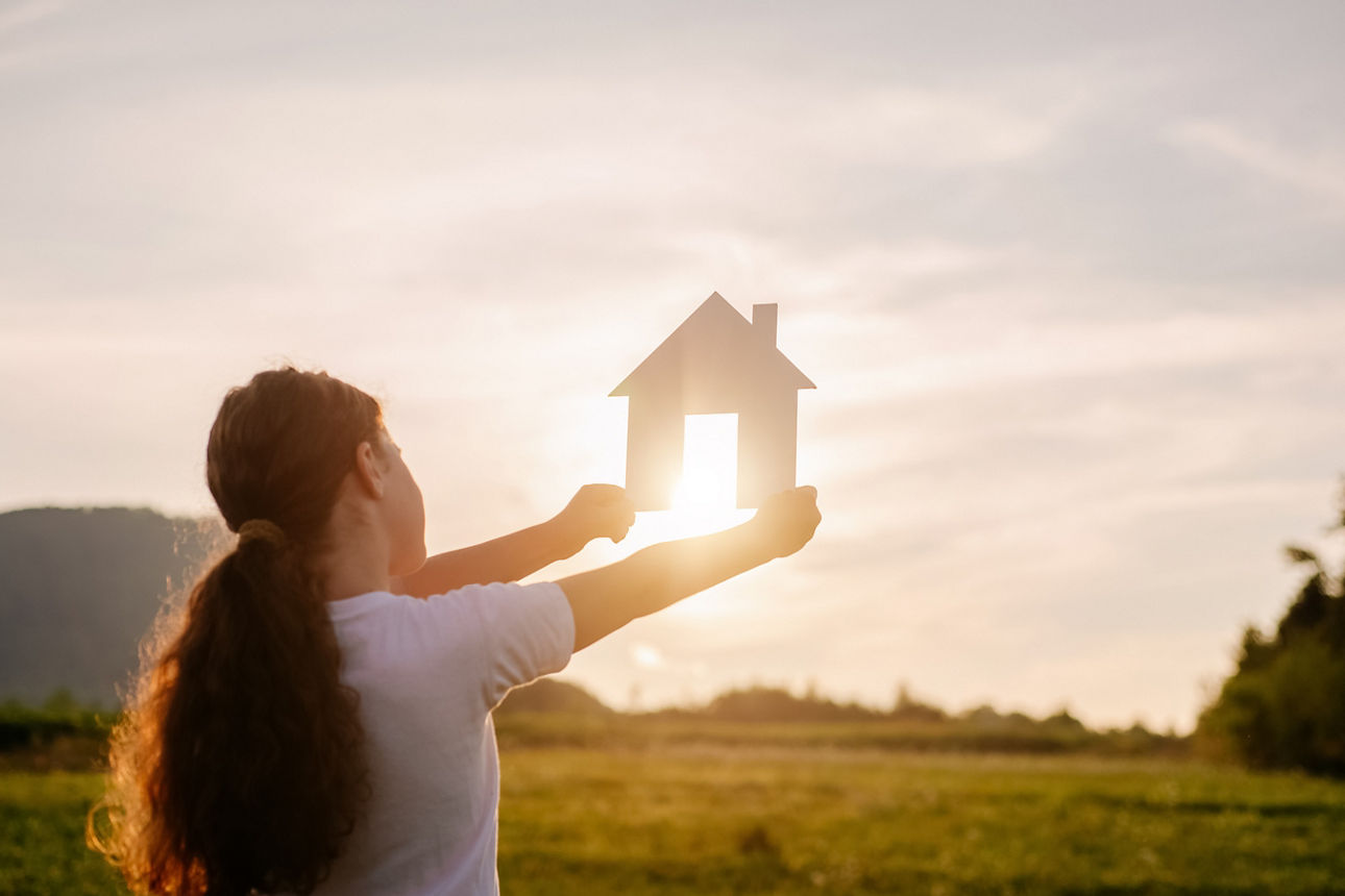 Frau in der Natur hält ein Modellhaus in die Sonne