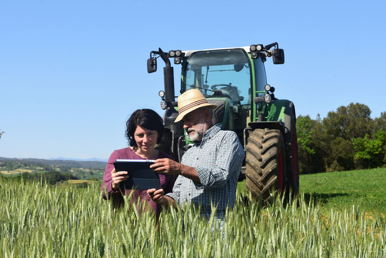 Ein Paar Landwirte steht vor ihrem Traktor und schaut auf ein Tablet.