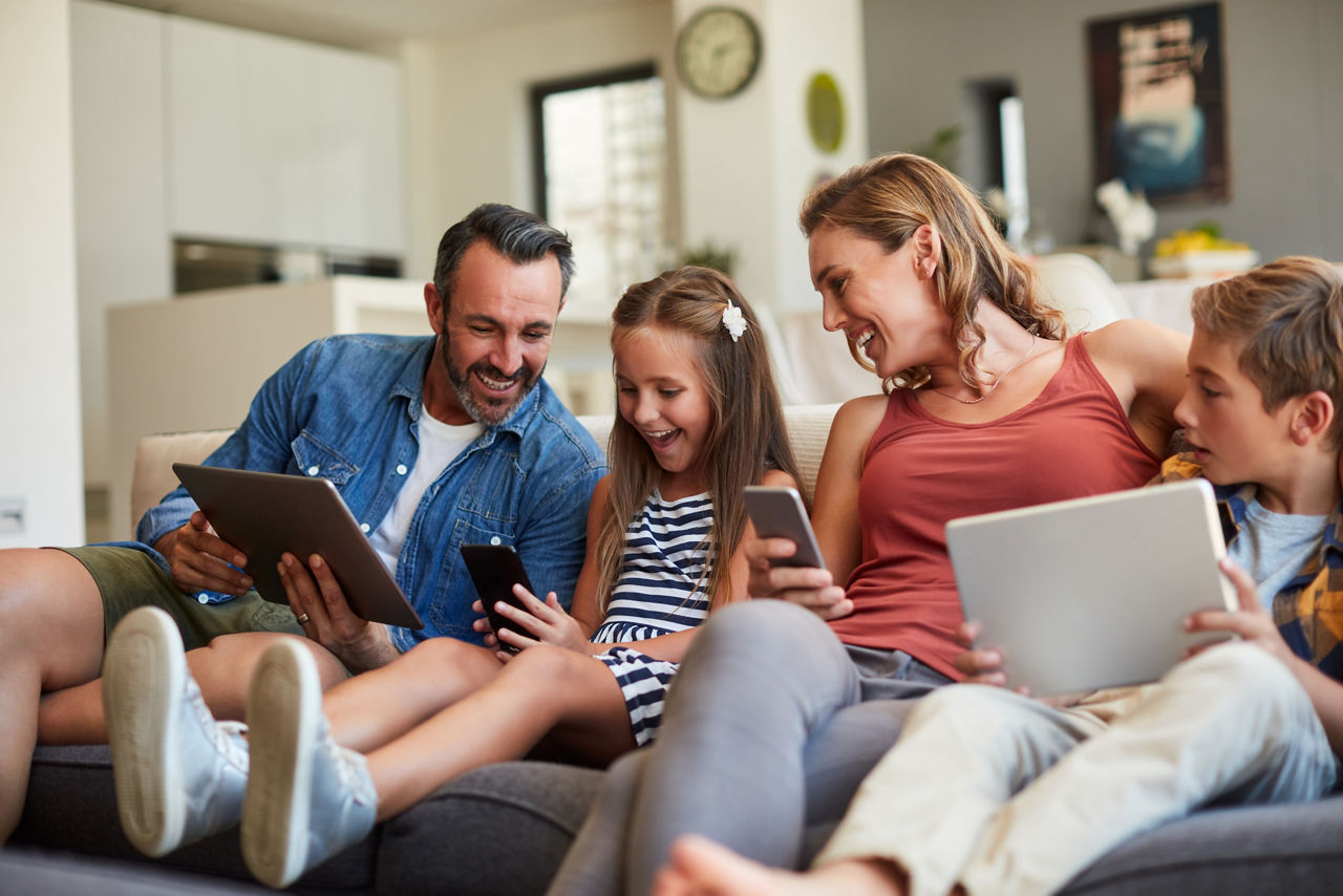 Glückliche Familie sitzt auf Couch und nutzt Smartphones und Tablets