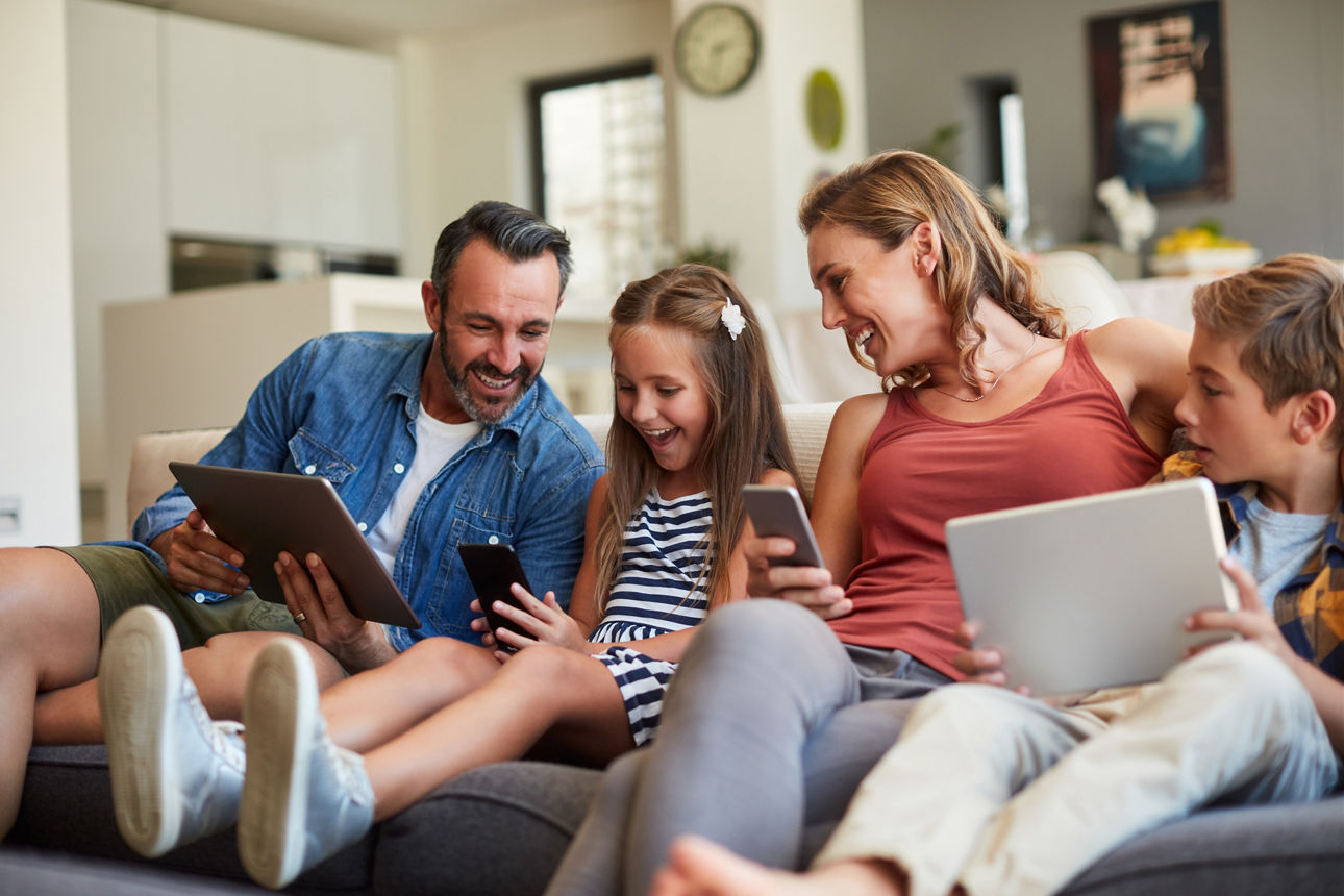 Glückliche Familie sitzt auf Couch und nutzt Smartphones und Tablets