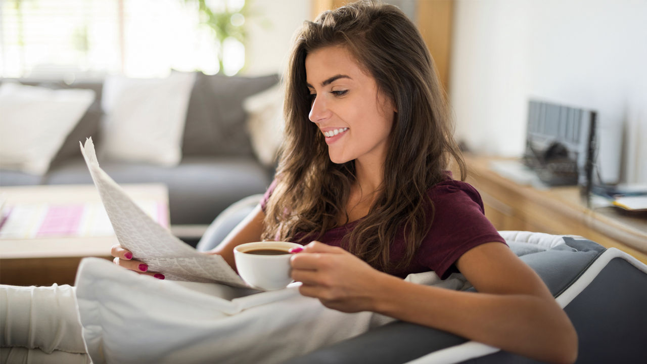 Eine junge Frau mit einer Tasse Kaffee liest Zeitung