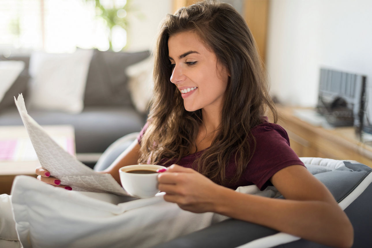 Eine junge Frau mit einer Tasse Kaffee liest Zeitung