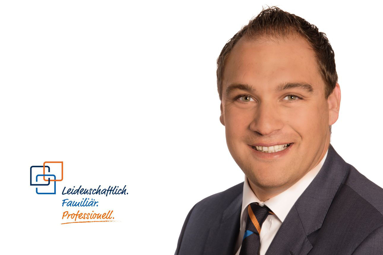 Porträt von Albert Joachim, einem lächelnden Mann mit kurzen dunklen Haaren im blauen Anzug mit orange-blau gestreifter Krawatte. Daneben das Firmenlogo und der Slogan "Leidenschaftlich. Familiär. Professionell."