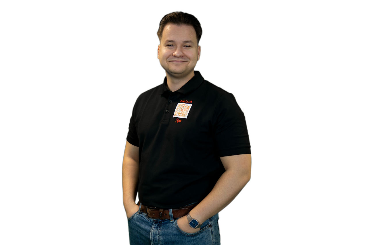 Junger Berufstätiger in einem schwarzen Poloshirt, hellen Jeans und einer Armbanduhr.