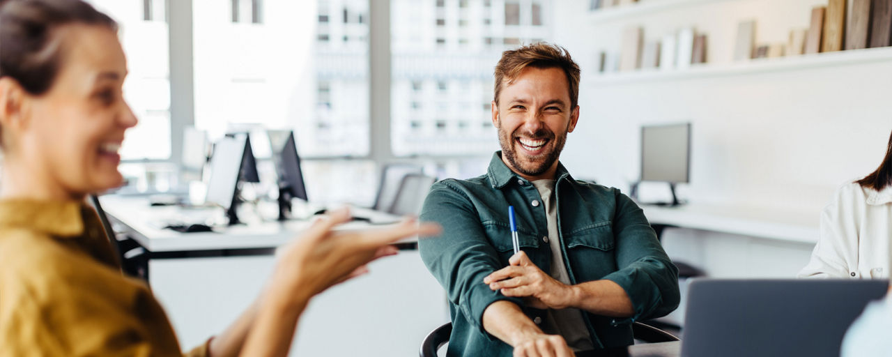 Mann und Frau mit Laptop lachend im Büro sitzend