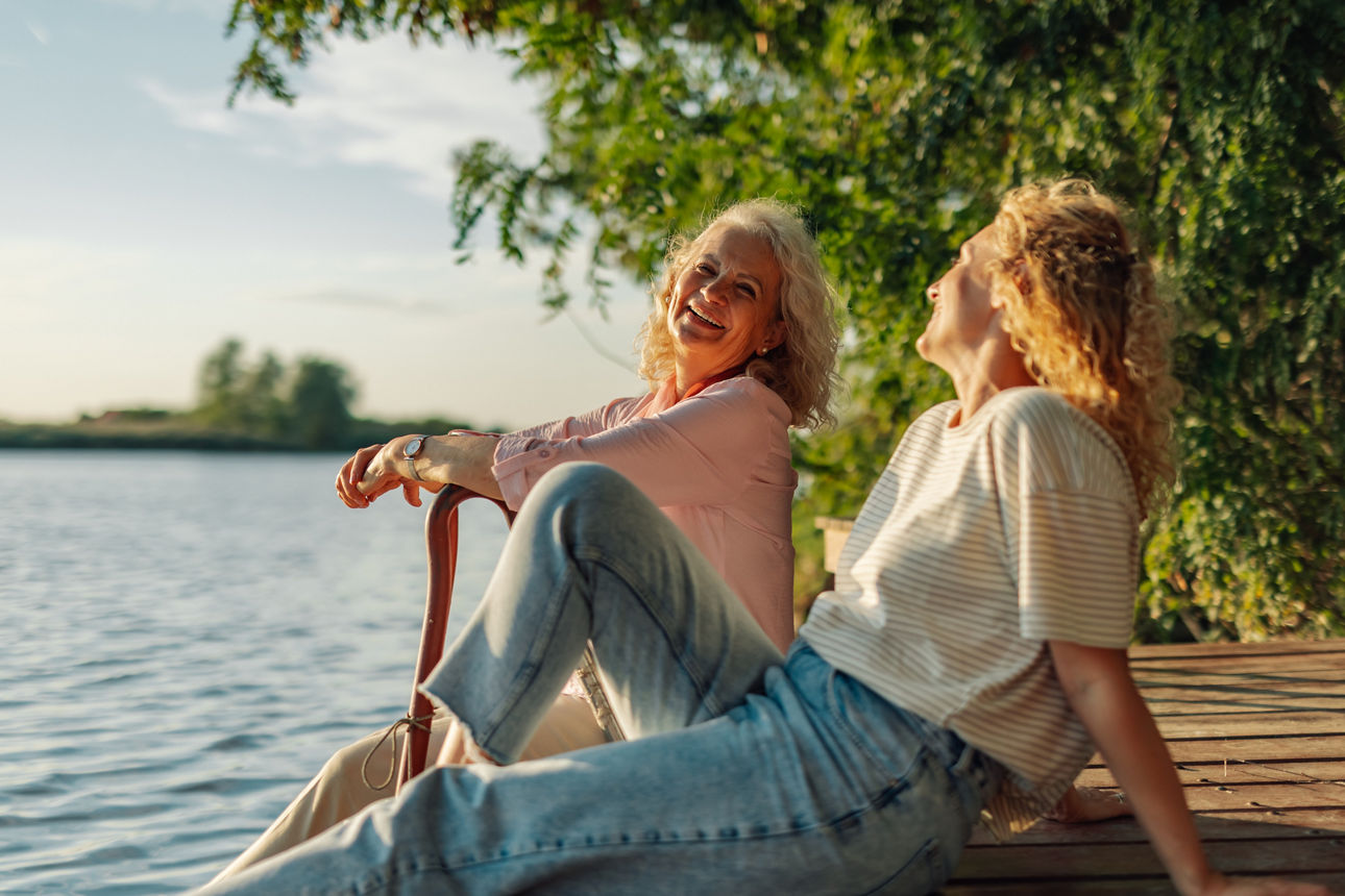 Two women sitting on a wooden dock, laughing and enjoying the sunset over the lake