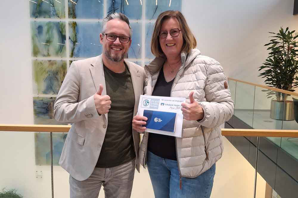 Zwei Personen lächeln in die Kamera, zeigen den Daumen hoch und halten gemeinsam ein Dokument in den Händen.