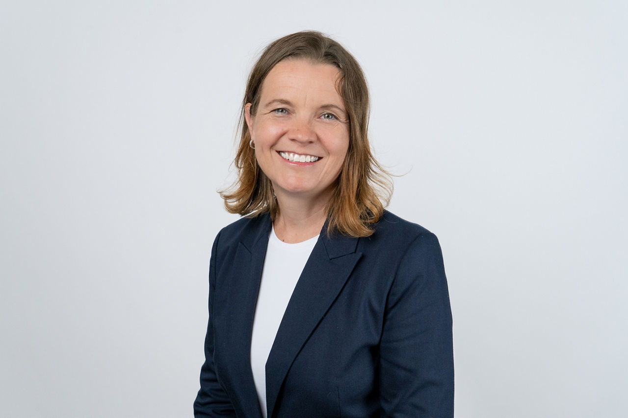 Foto unserer Vermögensberaterin Anja Kallies vor einem grauen Hintergrund mit einem schwarzen Blazer