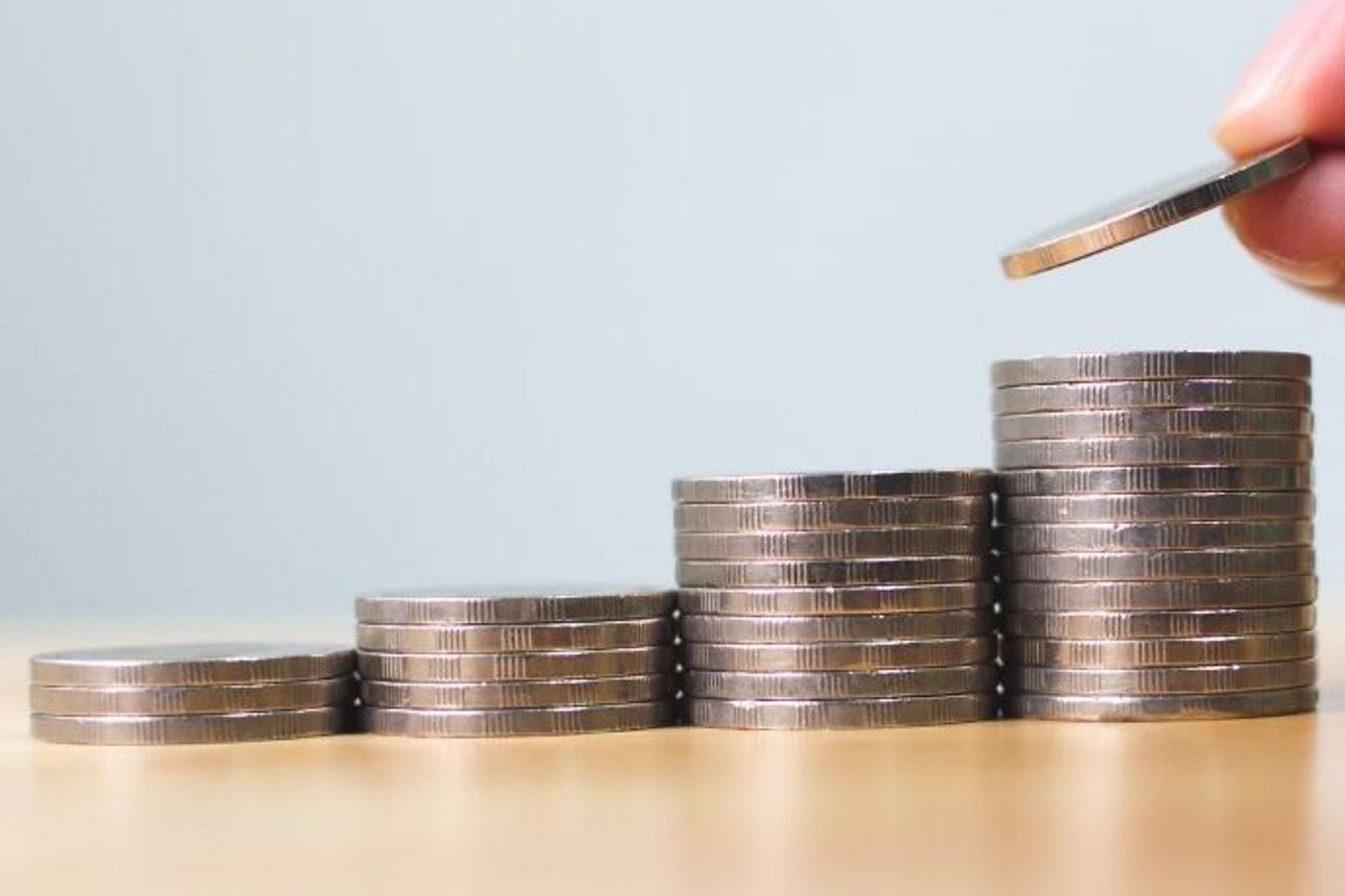 Vier Münzenstapel und Finger, die die Münzen stapeln