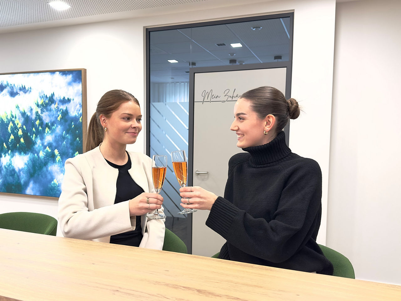 zwei junge Frauen stoßen mit Sektgläsern an einer Bar an