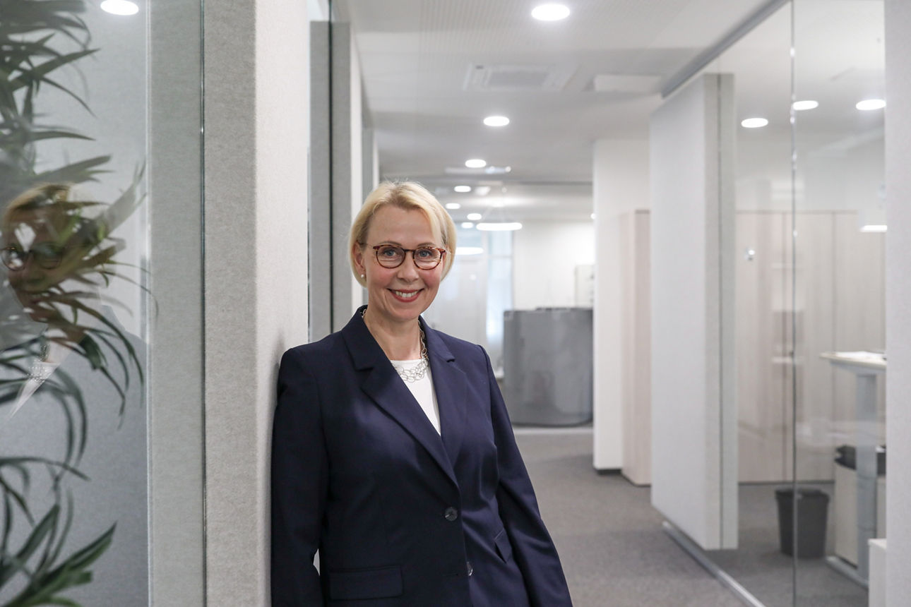 Frau steht im Gang angelehnt an die Wand und lächelt in die Kamera